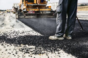 Worker operating asphalt paver machine during road construction and repairing works Find Road Surfacing companies Kent